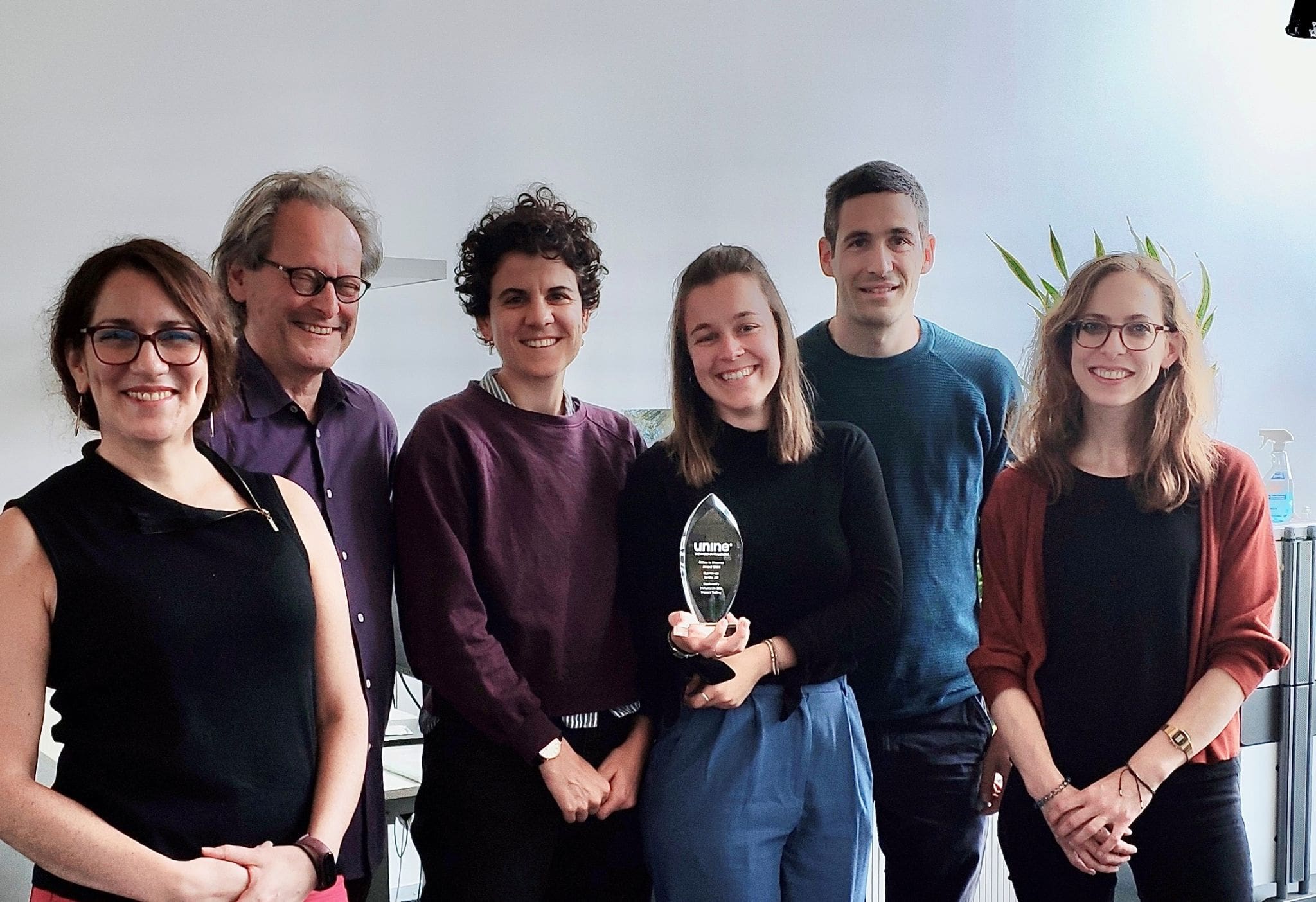 Group of six smiling Inrate team members standing together, with one holding an award trophy